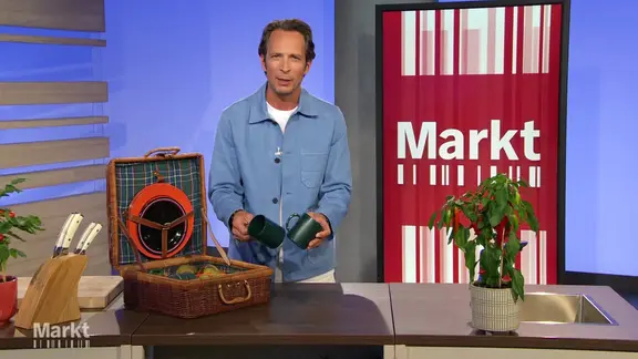 Moderator Jo Hiller im Studio von "Markt". Vor ihm auf dem Tisch ein Picknickkorb mit Kunststoff-Tellern und -Bechern sowie eine Pflanze und ein Messerblock.