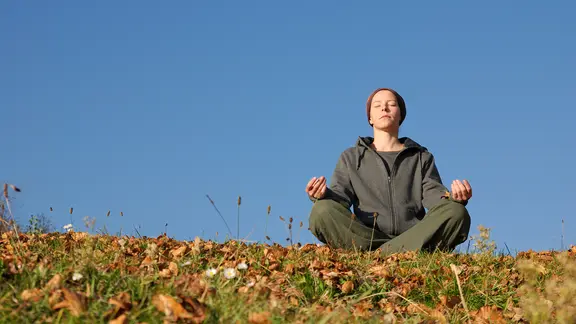 Frau sitzt im Lotusitz auf einer herbstlichen Wiese.