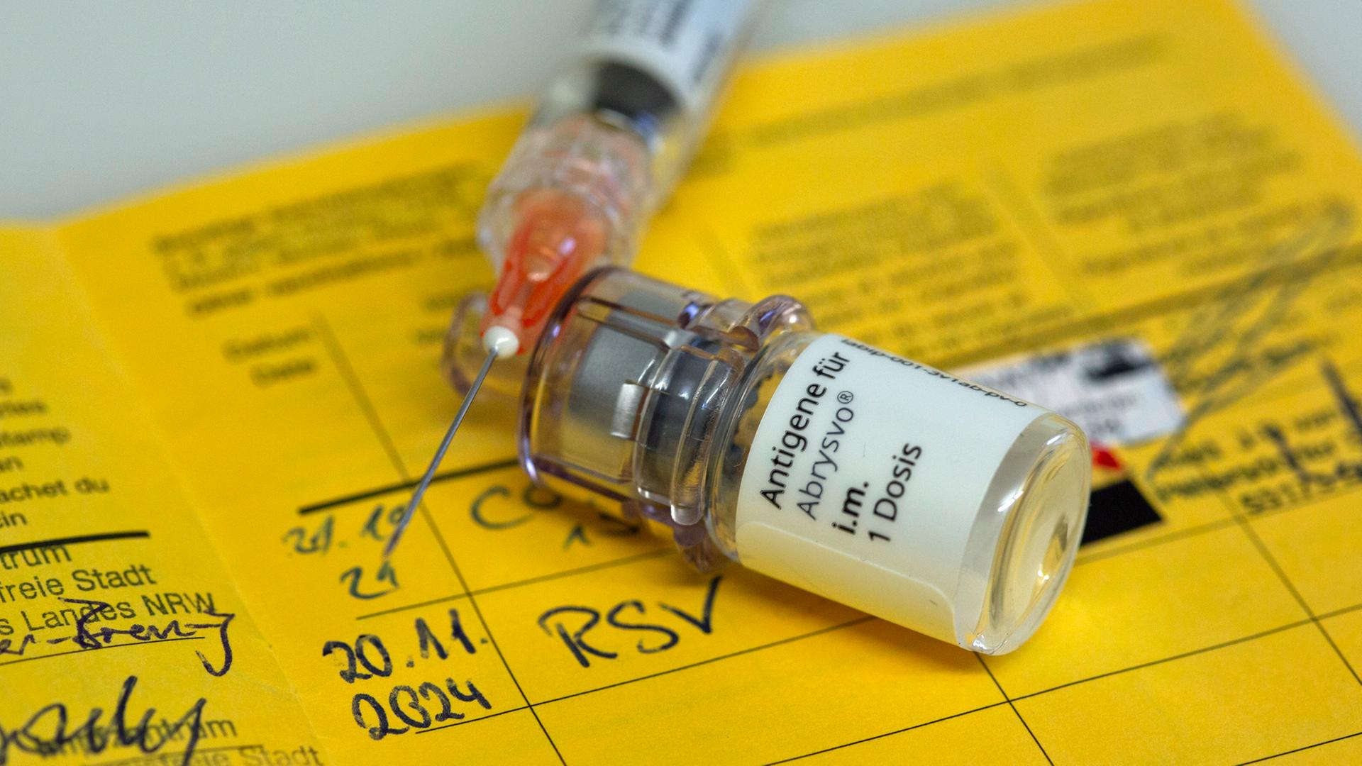 Eine Ampulle mit RSV-Impfstoff und eine Spritze liegen auf einem Impfpass. | picture alliance, Ulrich Baumgarten