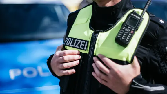 Ein Polizist, der hat seine Hände unter die Schutzweste der Uniform gesteckt hat.