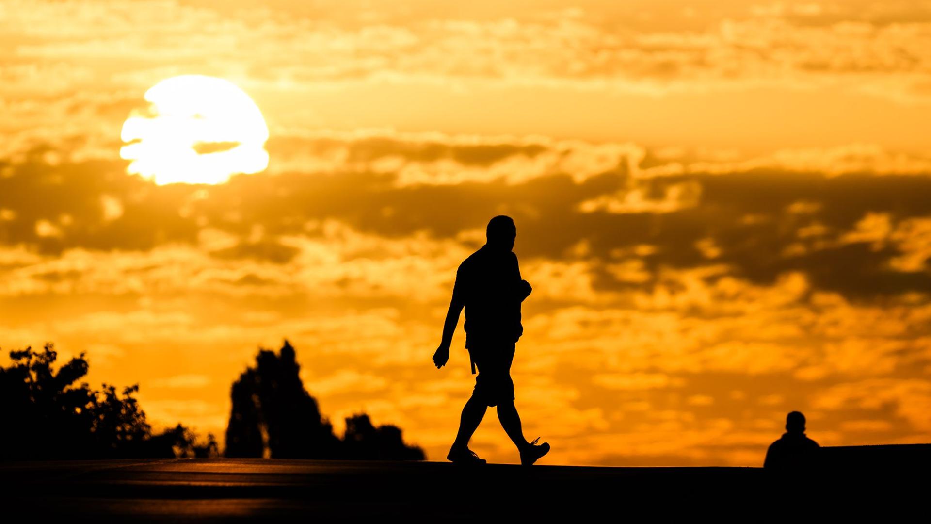 Ein Mann geht bei Sonnenaufgang über eine Straße in der Region Hannover. | dpa-Bildfunk/Julian Stratenschulte