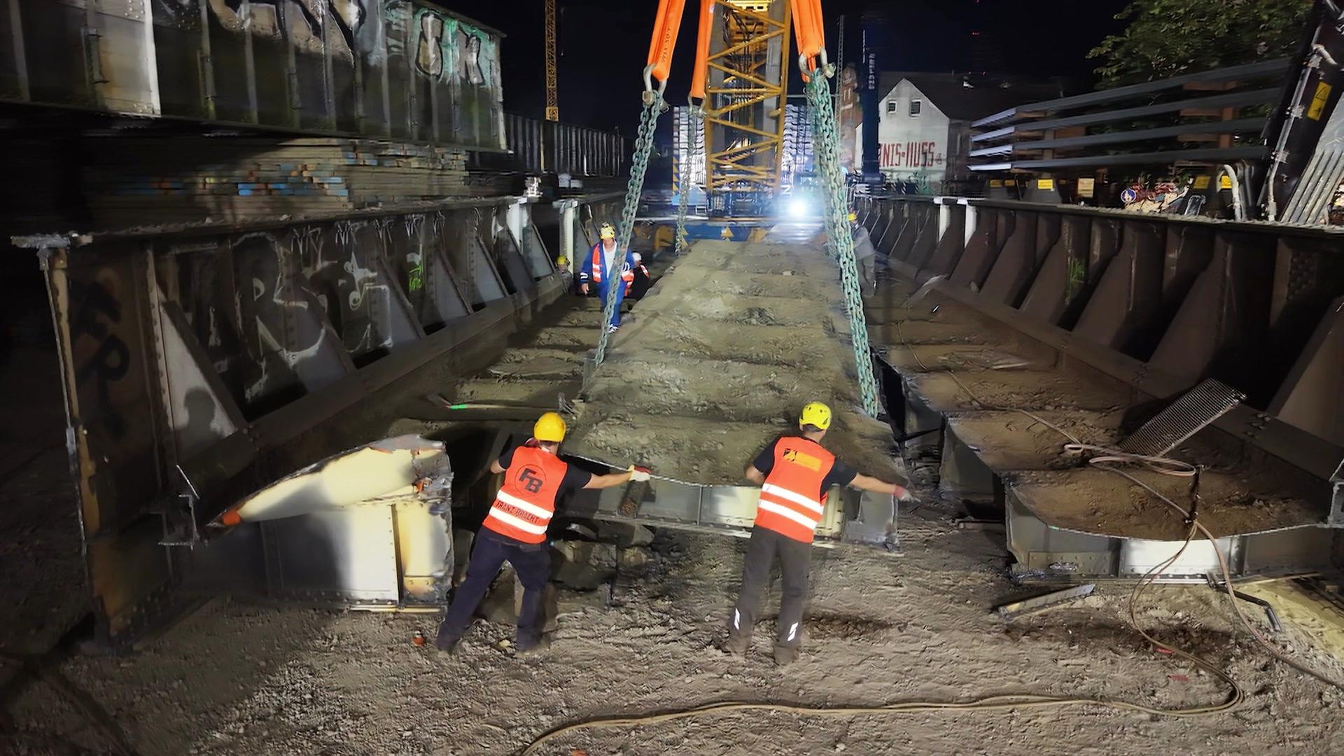 Zwei Bauarbeiter heben ein schweres Segment der alten Sternbrücke an.  | Screenshot