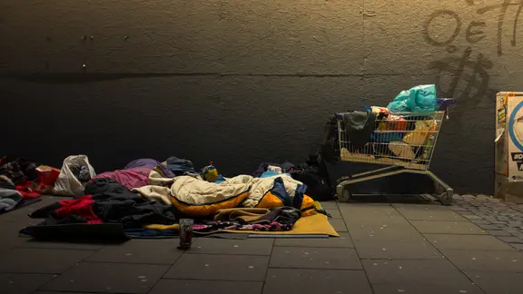 Ein Schlafplatz auf der Straße, mit Schlafsäcken und einem Einkaufswagen.