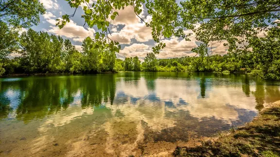 Blick über den Kiesteich in Lohnde bei blauen Himmel und vereinzelten Wolken.