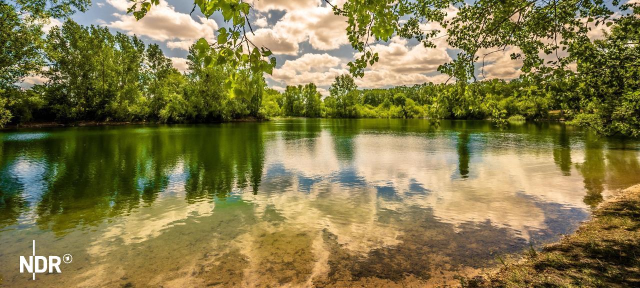 Blick über den Kiesteich in Lohnde bei blauen Himmel und vereinzelten Wolken.