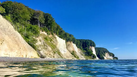Aus dem Blick vom Wasser sieht man die von der Sonne angeleuchteten Kreideklippen vom Nationalpark Jasmund.