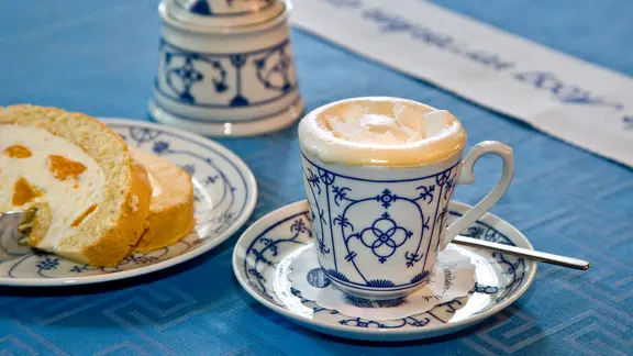 Kaffee mit Schuss: Auf einen Pharisäer gehört eine Sahnehaube. | picture-alliance / DUMONT Bildarchiv Eine Tasse Kaffeepunsch steht neben einem Stück Kuchen auf dem Tisch.