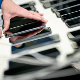 Eine Hand greift nach einem Smartphone, das neben weiteren Smartphones liegt. 