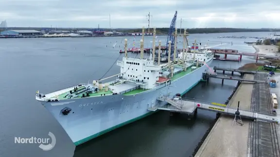 Blick auf ein großes historisches Schiff, dass an einer Kaimauer liegt.