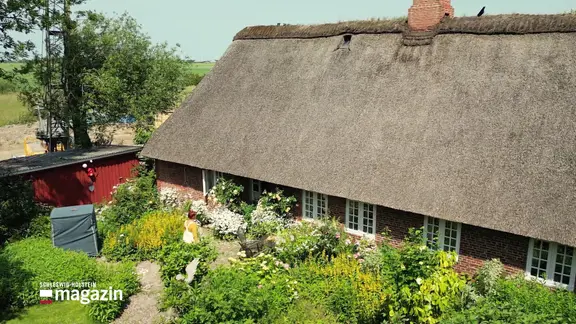Ein Haus mit Reetdach und einem großen Garten.