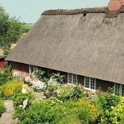 Ein Haus mit Reetdach und einem großen Garten.