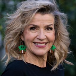 Eine Frau mit grünen Ohrringen und blonden Haaren lächelt in die Kamera.
