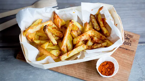 Ein Schälchen Pommes steht auf einem Holzbrett.