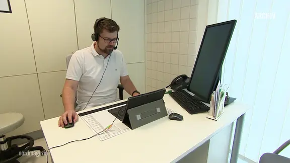 Ein Arzt sitzt mit Headset vor einem Computerbildschirm.