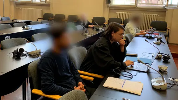 Ein Mann (l.) sitzt in einem Gerichtssaal in Hamburg. Er soll sein Kind entführt und den Flugbetrieb am Hamburger Flughafen stundenlang lahmgelegt haben.