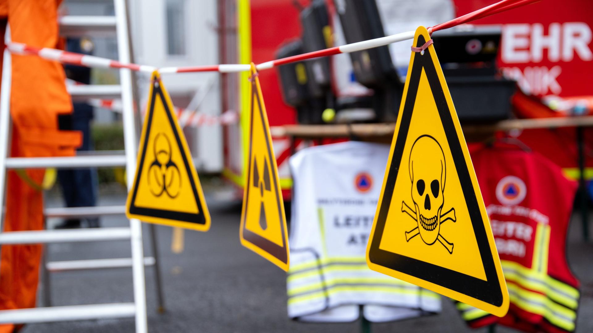 Bei einer Anti-Terror-Übung hängen die Warnzeichen vor Biogefährdung, Radioaktivität und giftigen Stoffen vor einem Feuerwehrfahrzeug. | picture alliance/dpa, Pia Bayer