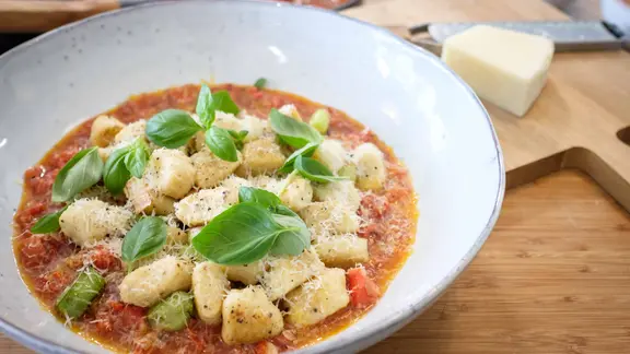 Gnocchi mit Tomatensoße, Parmesan und Basilikum auf einem großen Teller serviert.