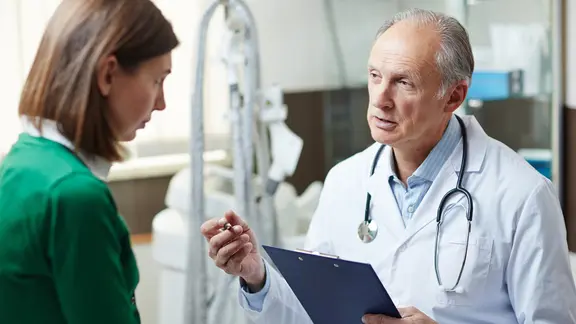 Arzt im Kittel mit Klemmbrett erklärt einer Patientin etwas (Bild: colourbox.de/Dmitrii Shironosov) | colourbox.de, Dmitrii Shironosov Arzt im Kittel mit Klemmbrett erklärt einer Patientin etwas (Bild: colourbox.de/Dmitrii Shironosov)