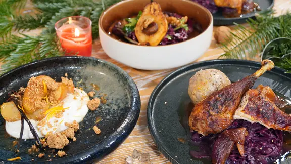 Bauernhuhn mit Knödeln und Rotkohl, Rotkohlsalat mit Birne und Vanillequark mit Äpfeln auf Tellern angerichtet.