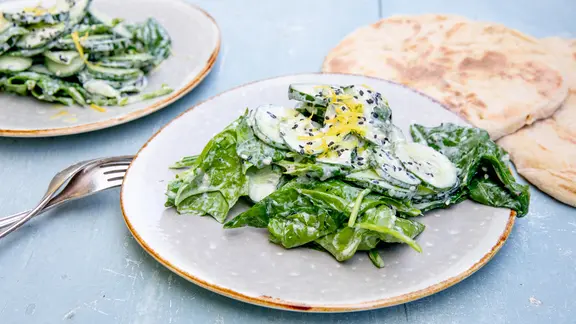 Gurken-Spinatsalat mit Joghurt und Sesam auf einem Teller serviert.