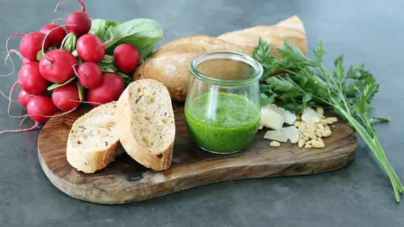 Zutaten für ein Radieschen-Blätter-Pesto und das Pesto auf einem Holzbrett.