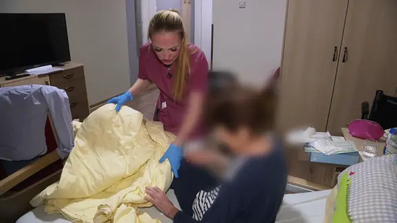 Eine junge Frau mit blonden Haaren und einem brombeerfarbenen Kittel.