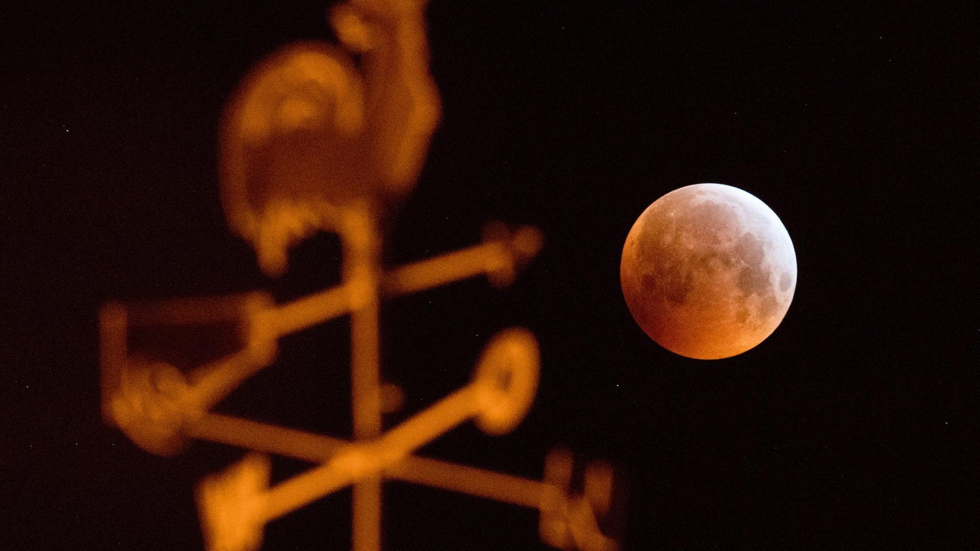 Der Blutmond steht am Himmel und im Vordergrund befindet sich ein Wetterhahn. | picture alliance/dpa | Julian Stratenschulte