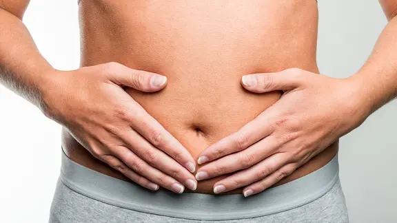 Eine Frau hält sich den nackten Bauch.