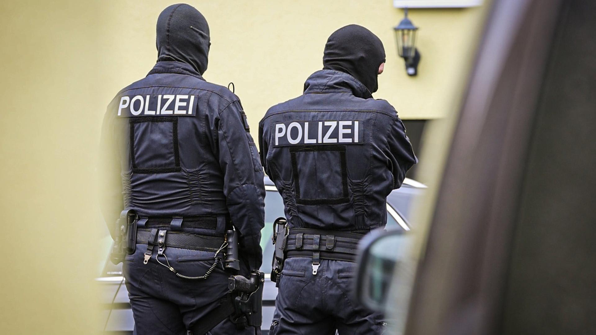 Zwei schwarz gekleidete Polizisten stehen mit dem Rücken zur Kamera vor einem Haus | picture alliance/dpa