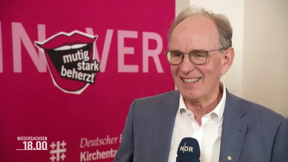 Ralf Meister, Landbischof von Niedersachsen, vor pinken Stellwand im Interview