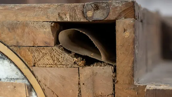 In einem Holzschrank steckt zusammengerolltes Blatt Papier.