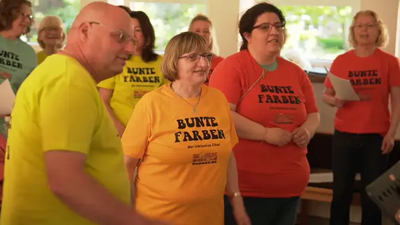 Mitglieder des Chores "Bunte Farben" stehen mit bunten T-Shirts aufgestellt zum Singen