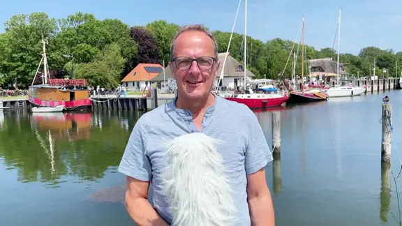Stefan Kreibohm stgeht mit Mikrofon am Hafen auf Hiddensee und erklärt das Wetter. 