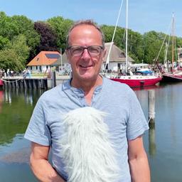 Stefan Kreibohm stgeht mit Mikrofon am Hafen auf Hiddensee und erklärt das Wetter. 