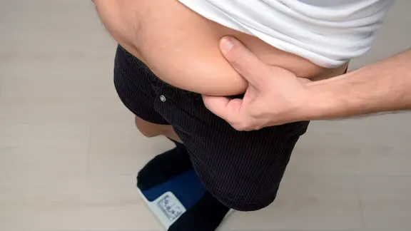 Ein Mann umfasst seinen Bauch mit den Händen.