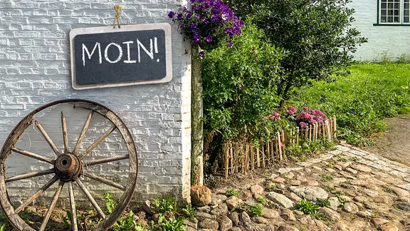 Auf einem Schild, das an einer Hauswand hängt, steht "MOIN".
