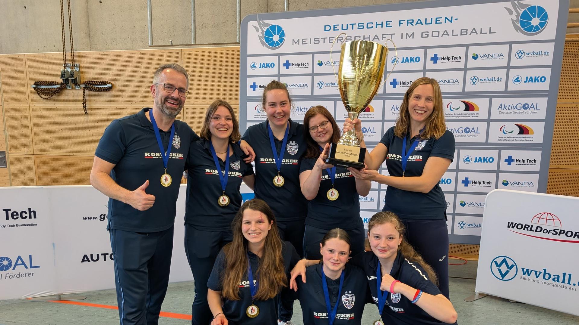 Eine Sportmannschaft posiert mit Medaillen, zwei Spielerinnen halten einen goldenen Pokal hoch. | RGC Hansa