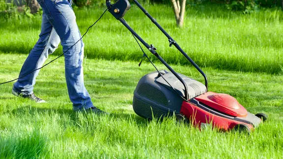 Person führt einen Rasenmäher auf einer Wiese