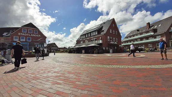 Der "Platz des himmlischen Friesen" im Westdorf lädt zu einem Bummel oder ein Eis in der Sonne ein. | NDR, Christina Maciejewski Urlauber auf dem "Platz des himmlischen Friesen" auf Baltrum