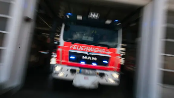 Ein Feuerwehrfahrzeug in Unschärfe fährt aus dem Hallentor einer Feuerwache.