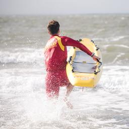 Ein Rettungsschwimmer läuft mit einem Rettungsbrett ins Meer.