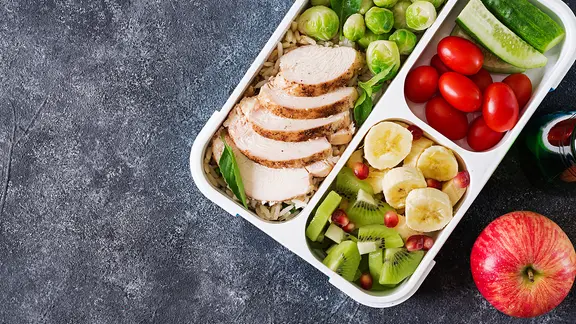 Hühnerfilet, Reis, Rosenkohl, Gemüse und Obst auf grauem Steinhintergrund