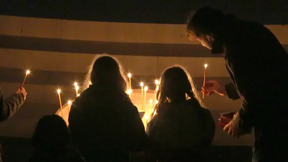 In der Nacht zum Ostersonntag tragen Christen das Licht in die dunklen Kirchen. | imago images / epd Mehrere Menschen stellen in einer dunklen Kirche Kerzen auf.
