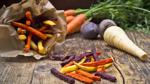 Alte Gemüsesorten wie Pastinake, Rote Bete und Möhren, teilweise geschnitten und frittiert, liegen auf einem Tisch.