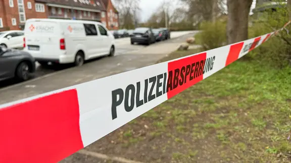 Ein rot-weißes Flatterband mit dem Schriftzug Polizeiabsperrung hängt zwischen Bäumen in Kiel-Elmschenhagen.