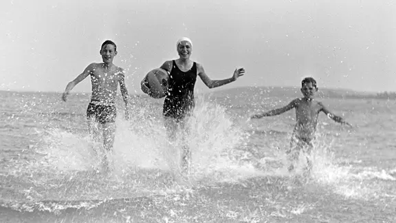 Eine junge Frau tobt mit zwei Jungen und einem Wasserball im Meer, Deutschland 1939.