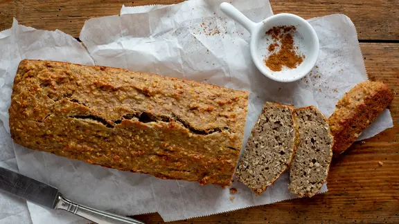 Ein angeschnittenes Bananenbrot und ein Schälchen Zimt liegen auf einem Tisch.