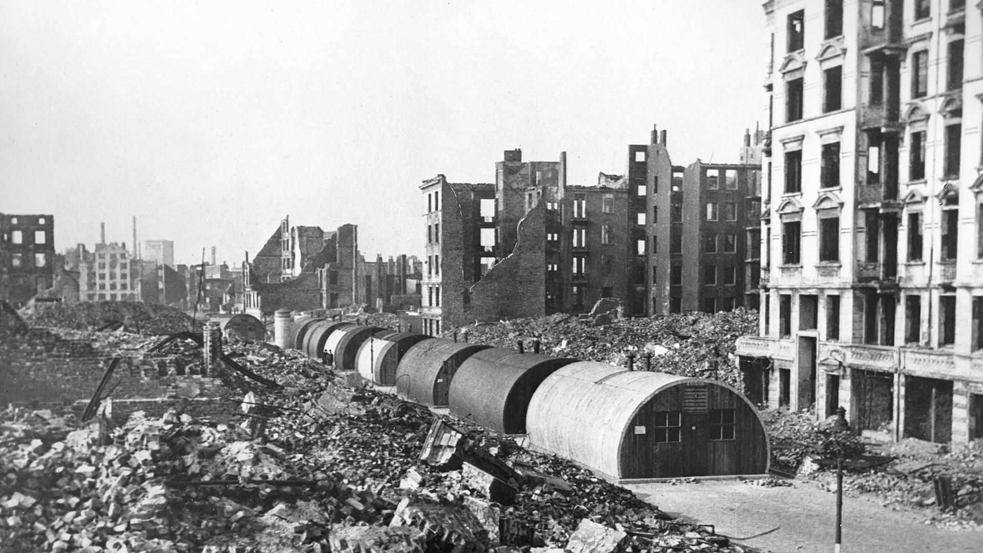 Vor Ruinen ausgebombter Wohnhäuser in Hamburg stehen Behelfsheime, sogenannte Nissenhütten. | picture-alliance/ dpa, Ulrich Mohr