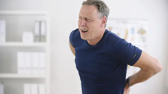 Ein Mann fasst sich mit schmerzverzerrtem Gesicht an den Rücken.