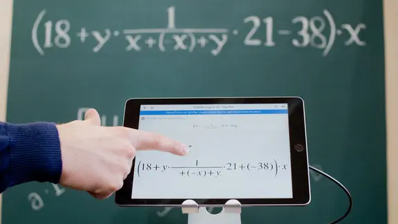 Ein Tablet mit einer mathematischen Formel vor einer Kreidetafel mit der gleichen Formel.